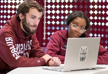 Two students working together at a laptop, one student in RIC sweatshirt